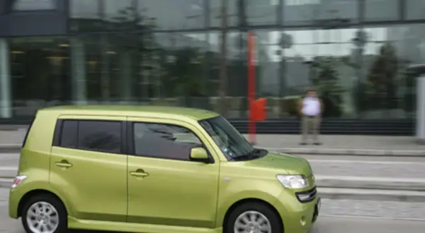 Zielony Daihatsu Materia jedzie ulicą obok nowoczesnego budynku.