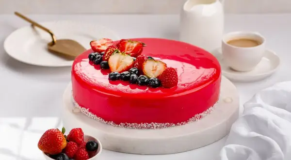 Torta rossa con glassa a specchio, decorata con fragole, mirtilli e lamponi. Un'opera d'arte culinaria.