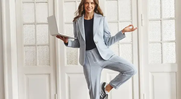 Kobieta w jasnoniebieskim garniturze i sneakersach, trzymająca laptopa, w pozie jogi. Idealny casual style damski do pracy i relaksu.