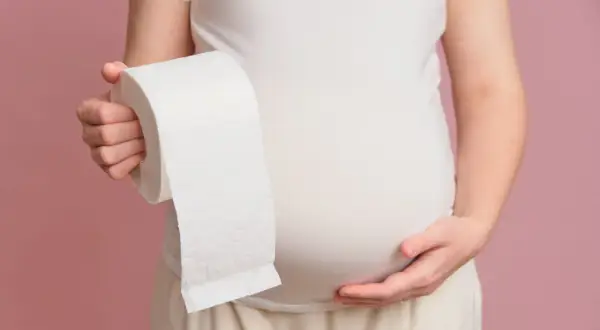 Ciężarna kobieta trzyma rolkę papieru toaletowego, symbolizującą problemy z biegunką w ciąży.