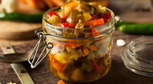 Un frasco de vidrio lleno de escabeche de verduras, con trozos de pimientos y zanahorias.