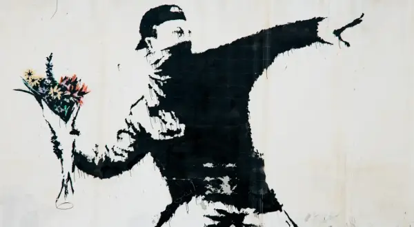 Czarny mural przedstawia zamaskowanego mężczyznę w czapce, rzucającego bukiet kolorowych kwiatów. To najładniejszy rysunek na świecie, pełen nadziei i buntu.