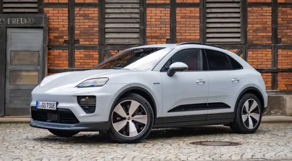 Biały Porsche Macan Electric na bruku, z ceglaną ścianą w tle. Sprawdź aktualną porsche macan cena.