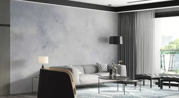 Nowoczesny salon z szarą kanapą i fotelami. Ściana ozdobiona tapetą imitującą beton, wykonaną z flizeliny.