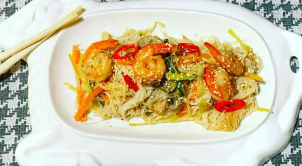 Deliziosi spaghetti di riso con gamberi succulenti e verdure croccanti, guarniti con semi di sesamo.