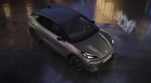 Nowoczesny Cupra Raval w ciemnoszarym kolorze, z czarnym dachem, stoi na mokrej nawierzchni, odbijając światła miasta.