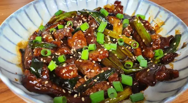 Un plat appétissant de boeuf aux oignons, garni de graines de sésame et d'oignons verts frais.