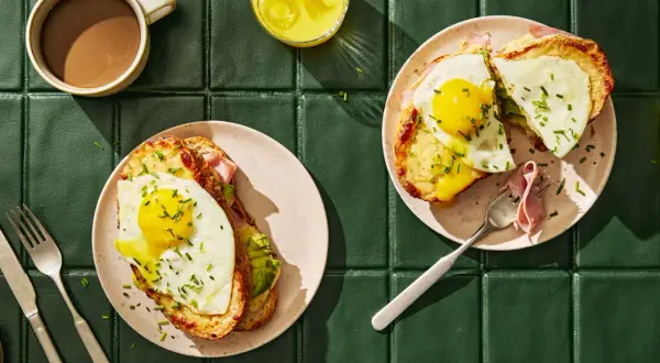 Två läckra croque madame med stekt ägg, ost och skinka, serverade med kaffe och juice.