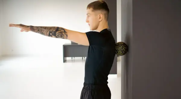 Mężczyzna z tatuażem na ramieniu masuje plecy piłką, celując w punkty spustowe.