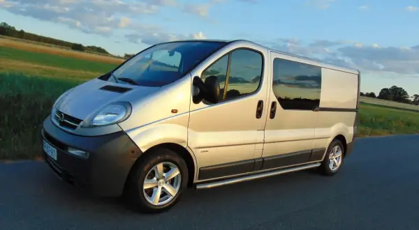 Srebrny Opel Vivaro 2.5 CDTI na drodze, zachód słońca. Wiele osób szuka opinii na forum o tym modelu.