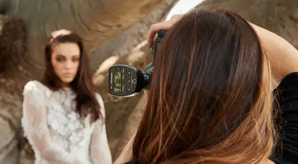 Fotografka z zimną stopką na aparacie celuje w modelkę w białej sukni.