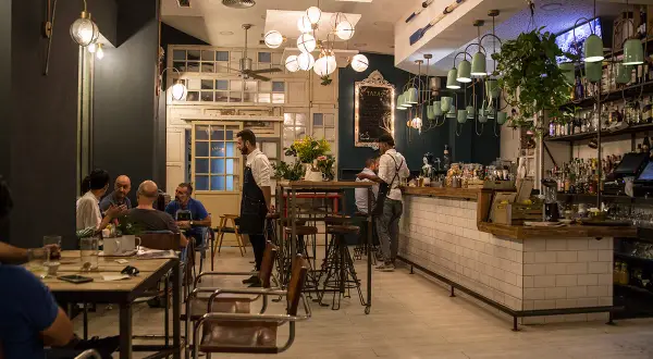Gente disfrutando de tapas en Almería, con camareros sirviendo y un ambiente acogedor.