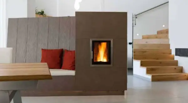 Moderner Wohnraum mit gemütlicher Sitzbank, Kamin und Holztreppe. Die Pelletheizung im Kamin sorgt für Wärme, die Vorschriften sind eingehalten.