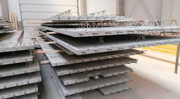 Stos prefabrykowanych płyt betonowych z widocznym zbrojeniem, przypominającym delikatny filigran.