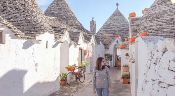 Una donna passeggia tra i trulli di Alberobello, un'icona di cosa vedere in Puglia. Le case coniche e i colori vivaci creano un'atmosfera magica.