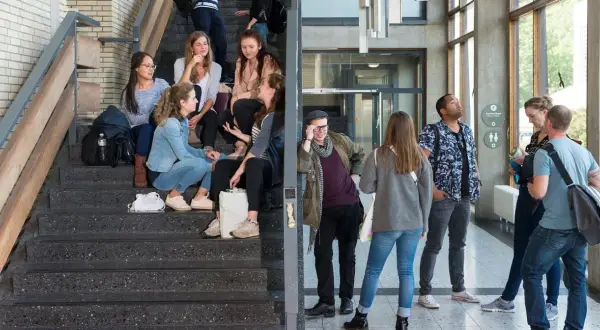 Studenten auf Treppen und im Flur. Eine Gruppe junger Leute, die sich auf einer Treppe unterhalten, vielleicht nach einem Kurs im berufsbegleitenden Studium Berlin.