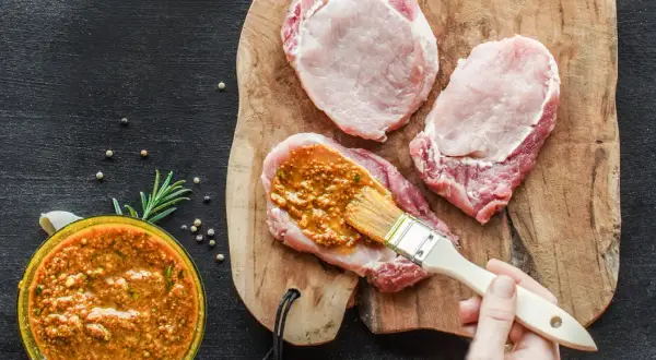 Frisches **Schweinefleisch marinieren** für zarte Steaks. Eine würzige Marinade wird mit einem Pinsel aufgetragen.
