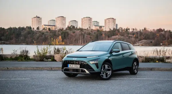 Grön Hyundai Bayon parkerad vid en sjö med stadssiluett i bakgrunden. En perfekt bil för en testkörning i skymningen.