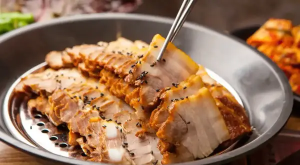 Plasterki soczystej wieprzowiny, posypane czarnym sezamem, idealne na dietę samo mięso. Obok widać kimchi.