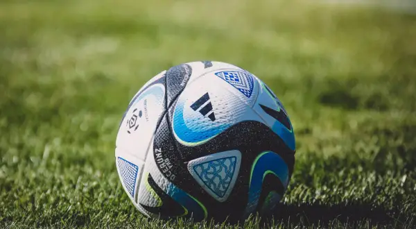 Piłka nożna na zielonej trawie, z widocznymi detalami i logo Adidas.
