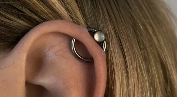 Obrączka z białym kamieniem, czyli orbital piercing, zdobi ucho.