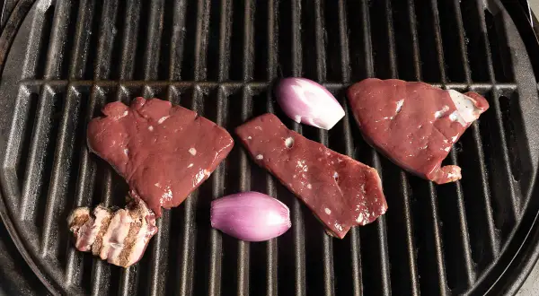 Rohe Leberstücke und Schalotten liegen bereit zum leber grillen auf einem heißen Rost.