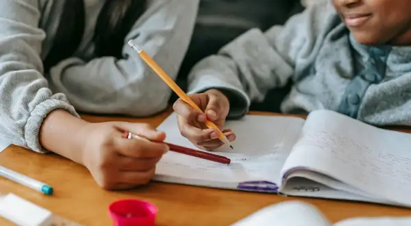 Dos niños concentrados en su dictado de 3 primaria, escribiendo en un cuaderno con lápices.