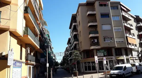 Calle soleada en Les Roquetes del Garraf, con edificios residenciales y comercios.
