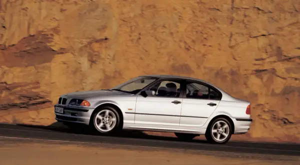 Srebrne bmw e46 330i sunie po drodze na tle skalistego, pomarańczowego zbocza.