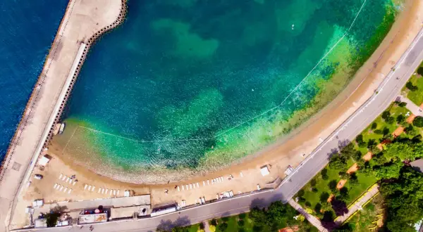 Vista aerea di una spiaggia e di un molo a Istanbul, dove c'è il mare turchese e una strada costiera con un parco verde.