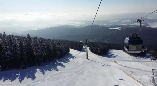 Trasa narciarska w Janskie Łaźnie, kolejka linowa wznosi się nad ośnieżonymi drzewami i stokiem.