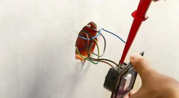Instalator podłącza podwójny włącznik światła, używając próbnika do przewodów. Pokazano, jak podłączyć włącznik światła podwójny trzy przewody.