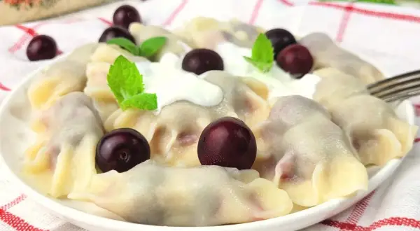 Pyszne pierogi z wiśniami, polane śmietaną i ozdobione świeżymi wiśniami i miętą. Letnia uczta na talerzu.