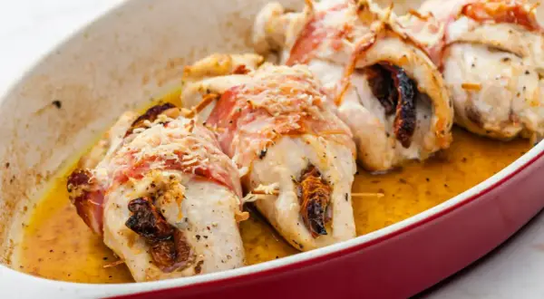 Pyszne roladki z kurczaka zawinięte w boczek, zapieczone z suszonymi pomidorami i posypane parmezanem, w sosie własnym.
