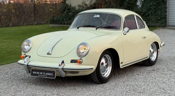 Klasyczny kremowy Porsche 356 z czerwoną tapicerką, zaparkowany na żwirowej nawierzchni.