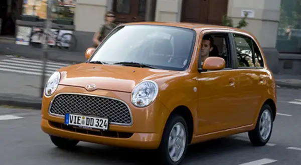 Pomarańczowy Daihatsu Trevis z kierowcą za kierownicą jedzie ulicą.