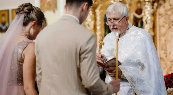 Para Młoda klęczy przed kapłanem podczas cichego ślubu kościelnego bez mszy. Kapłan trzyma krzyż i świecę.