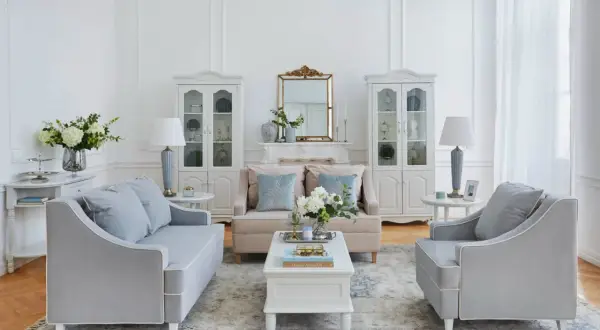 Salotto in stile shabby con divani grigi, poltrone, tavolino bianco, specchio dorato e vetrine.