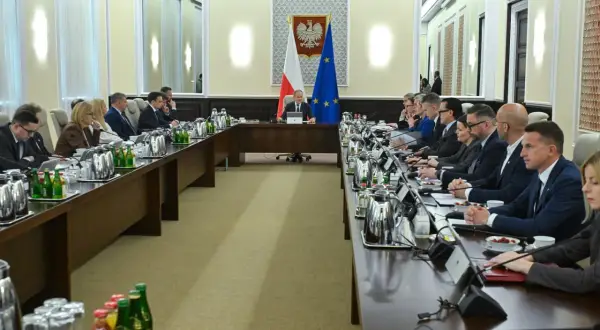 Uczestnicy spotkania przy długim stole, dyskutują o budżetowym deficycie. Na stole napoje i dokumenty.