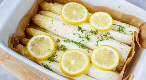 Frischer weißer Spargel im Backofen mit Zitronenscheiben und Petersilie, bereit zum Genießen.
