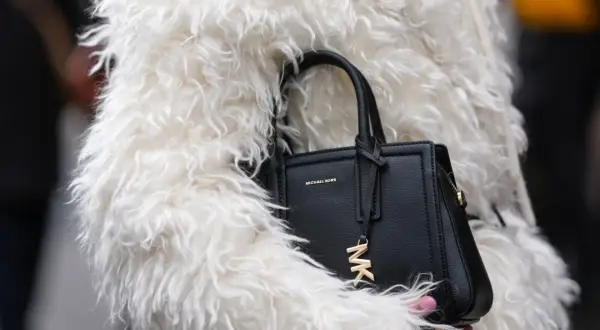 Czarna torebka Michael Kors z logo MK, otulona w białe futro. To marka znana z luksusowych akcesoriów.