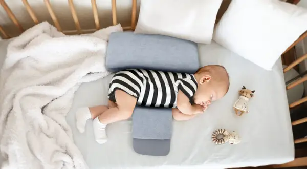 Noworodek śpi na boku, podtrzymywany przez poduszkę klin. Czy poduszka klin jest bezpieczna dla noworodka? Tak, jeśli jest używana zgodnie z zaleceniami.