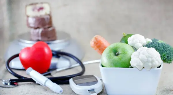 Zdrowe jedzenie, jak jabłko i warzywa, wspiera dietę mitochondrialną. Obok serce, stetoskop i glukometr symbolizują troskę o zdrowie.