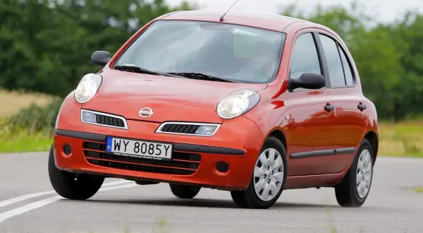 Pomarańczowy Nissan March z tablicą rejestracyjną WY 8085Y jedzie po drodze wśród zieleni.