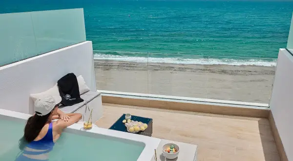 Mujer en bañera de hidromasaje con vista al mar, con presillas bajas en su traje de baño, disfruta de una bebida refrescante.