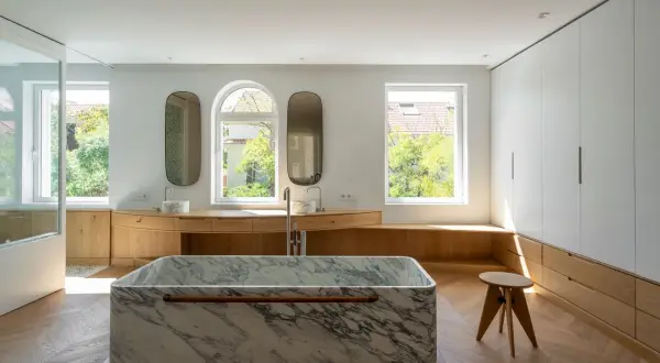 Baño moderno con bañera de mármol, lavabos y armarios de madera. Un ejemplo de reformas casas de pueblo con estilo.