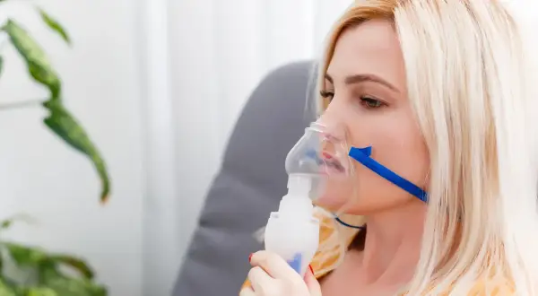 Kobieta z maską nebulizatora, wdychająca sól fizjologiczną.