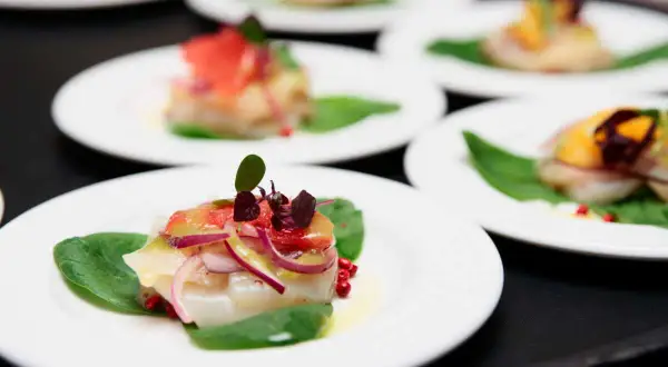 Carpaccio de saint jacques frais, garni de pamplemousse, oignons rouges et pousses sur des feuilles d'épinards.