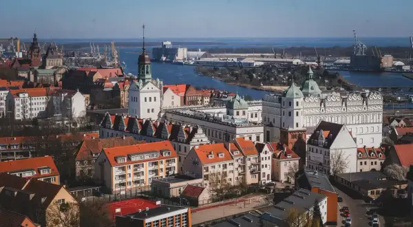 Widok na zamek i port w Szczecinie. Zabytkowe budowle z czerwonymi dachami kontrastują z błękitem wody i nieba.