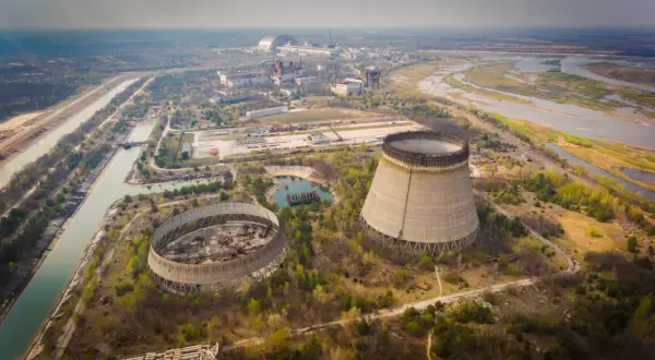 Widok na opuszczoną elektrownię atomową, gdzie doszło do katastrofy w Czarnobylu. Widać niedokończone wieże chłodnicze i rozległy teren.
